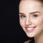 Smiling woman receiving Diamond Glow in Leesburg, FL, with clear skin and blue eyes, light brown hair pulled back, against a black background.