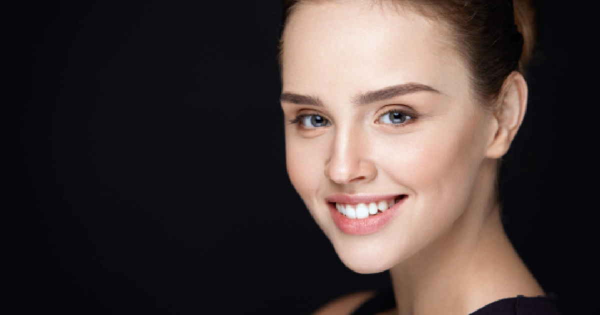 Smiling woman receiving Diamond Glow in Leesburg, FL, with clear skin and blue eyes, light brown hair pulled back, against a black background.