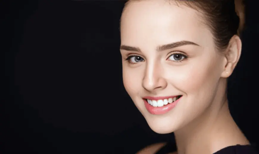Smiling woman receiving Diamond Glow in Leesburg, FL, with clear skin and blue eyes, light brown hair pulled back, against a black background.