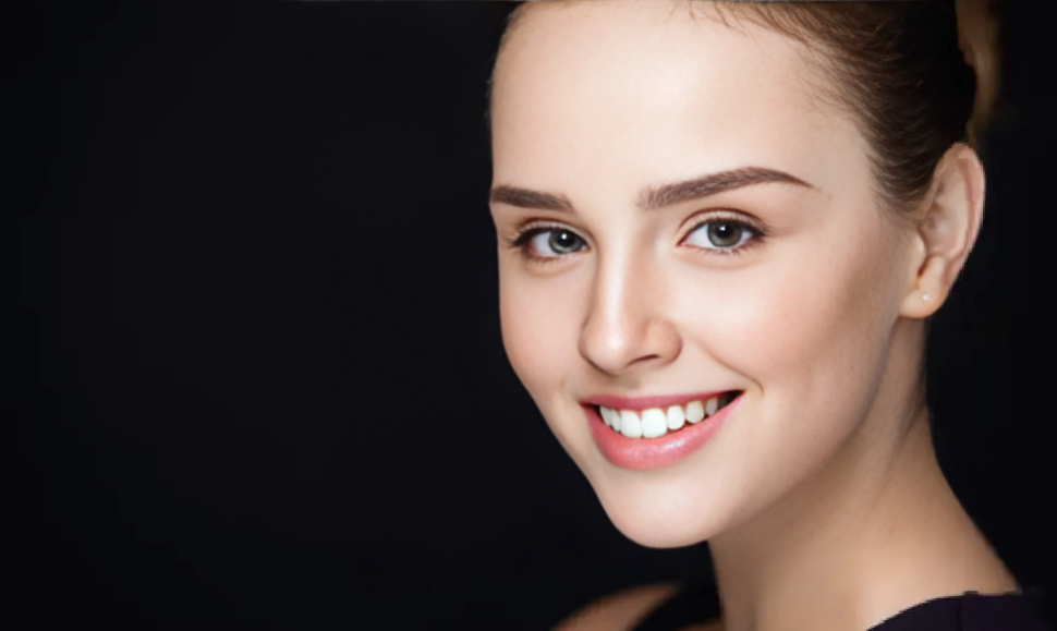 Smiling woman receiving Diamond Glow in Leesburg, FL, with clear skin and blue eyes, light brown hair pulled back, against a black background.